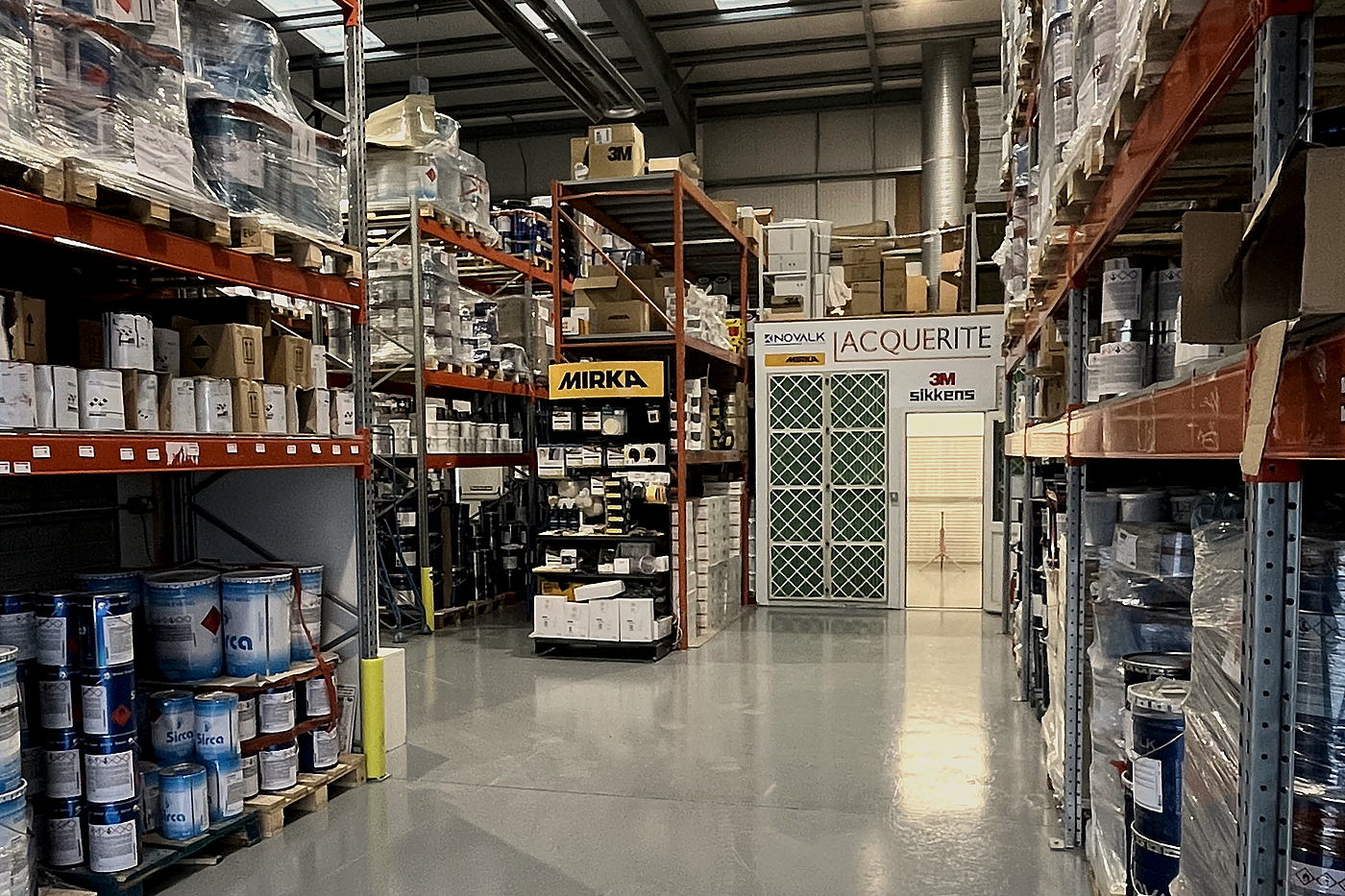 Warehouse aisle in Tullamore with Sirca stock, a Mirka stand and the Lacquerite mixing room ahead